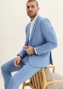 Er trägt einen eleganten, hellblauen Anzug über einem frischen weißen Hemd.