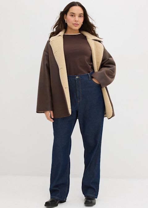 Braune Jacke mit hellem Kragen, passend zu dunklem Oberteil und Jeans.