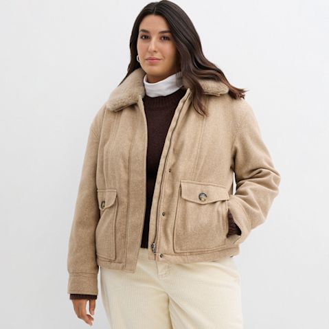 Beige Winterjacke mit Kragen, darunter ein brauner Pullover und weißer Rollkragenpullover.