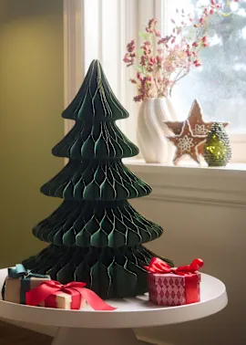 Ein grüner Papier-Weihnachtsbaum, festliche Geschenke und ein elegantes Kissen zieren den Raum.