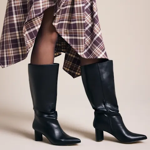 Modischer Auftritt: Karierter Rock, schwarze Strumpfhose und elegante schwarze Stiefel.