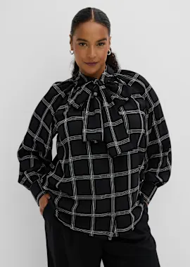 Elegante schwarze Bluse mit weißem Karomuster und großer Halsschleife, dazu schwarze Hose.