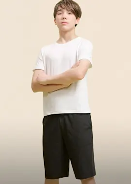 Junge trägt ein schlichtes weißes T-Shirt und dunkle kurze Hosen.