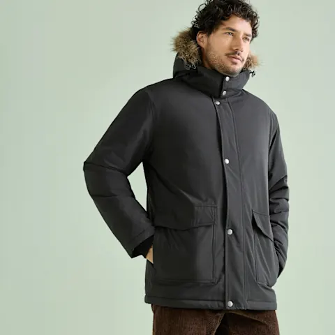 Ein Mann trägt einen robusten schwarzen Parka mit Fellkapuze und braune Cordhose.