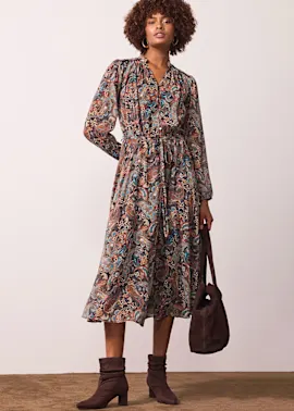 Gemustertes Midi-Kleid mit langen Ärmeln, Gürtel und V-Ausschnitt. Dazu braune Stiefeletten und Handtasche.