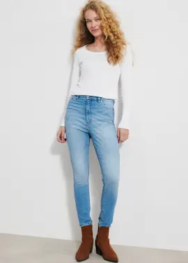 Sie trägt ein schlichtes weißes Oberteil, helle Jeans und braune Stiefeletten.