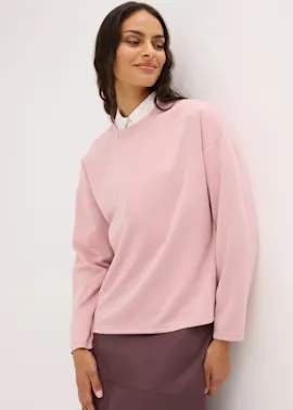 Rosa Oversize-Sweatshirt über weißem Hemd, dazu ein eleganter dunkler Rock.