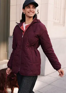 Dunkelrote Steppjacke, darunter ein roter Strickpullover, schwarze Cap und silberne Ohrringe.