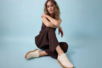 Die Frau trägt einen schicken braunen Jumpsuit und passende beige Sneaker.
