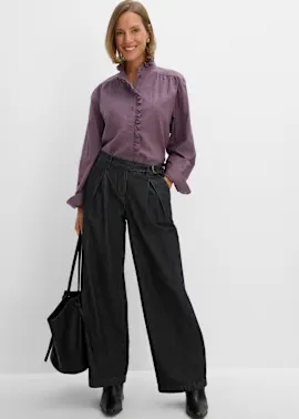 Schicke lila Rüschenbluse mit weiten, dunklen Jeans, dazu schwarze Stiefeletten und Shopper.