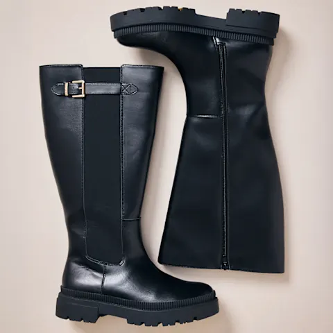 Zwei schwarze, kniehohe Stiefel mit markanter Profilsohle und Schnallendetail.
