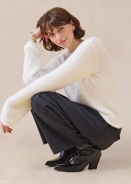 Flauschiger weißer Pullover kontrastiert mit eleganter schwarzer Hose und Schuhen.