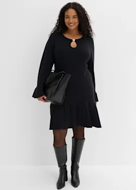 Elegantes schwarzes Kleid mit Ausschnitt, dazu Strumpfhose, kniehohe Stiefel und Handtasche.