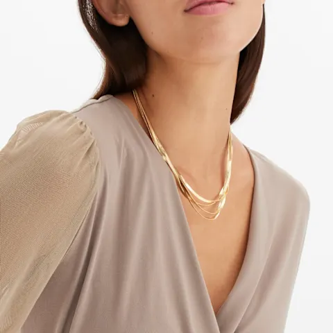 Elegantes Wickel-Oberteil mit transparenten Ärmeln, dazu goldene Halskette und Armband.