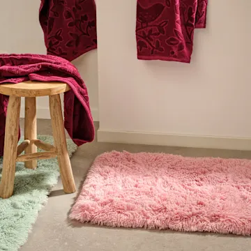 Weiche Badematte und rote Handtücher im Badezimmer.