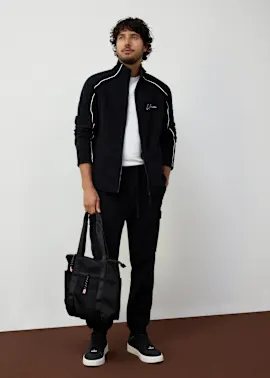Sportlicher Look mit schwarzer Trainingsjacke, weißem T-Shirt und passender Hose.