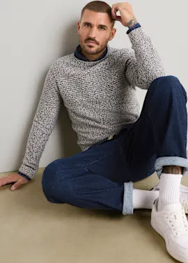 Grauer Strickpullover über blauem Hemd, dunkle Jeans, weiße Socken und Sneaker.