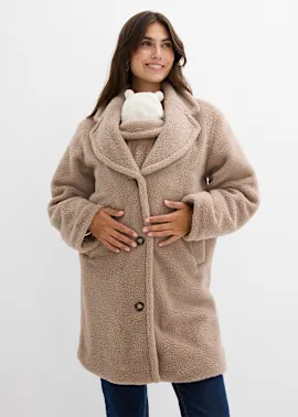 Eine lächelnde Frau trägt einen beigen, kuscheligen Oversized-Mantel über einem weißen Oberteil.