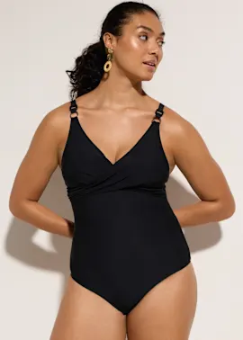 Elegante Frau präsentiert einen schwarzen Badeanzug mit Wickel-Optik und dekorativen Trägerringen.