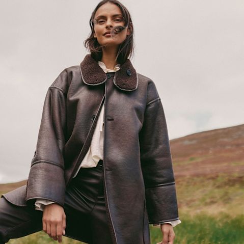 Eleganter brauner Ledermantel mit großem Kragen kombiniert mit ein helles Oberteil und dunkler Hose.