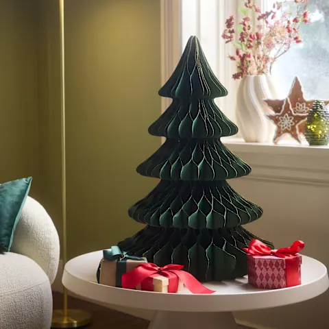 Grüner Faltweihnachtsbaum, Geschenke, gemütliches Sofa und winterliche Dekorationen am Fenster.