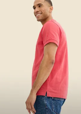 Er trägt ein leuchtend rotes Poloshirt und bequeme blaue Jeans.