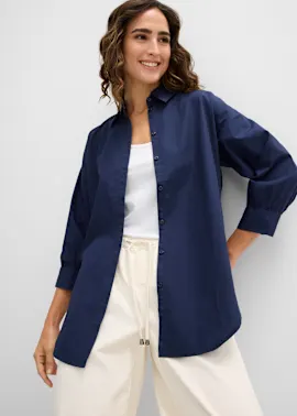 Die Frau trägt ein marineblaues Oversize-Hemd über einem weißen Top und helle Hose.