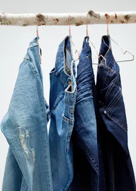 Jeans in verschiedenen Blautönen hängen an Bügeln auf einem Holzast.