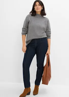 Grauer Stehkragenpullover, dunkle Jeans mit Nähten, braune Stiefeletten und Tasche.