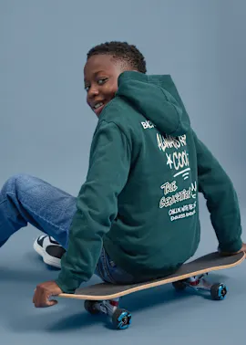 Grüner Hoodie mit Aufdruck, blaue Jeans und Sneakers für einen coolen Skater-Look.