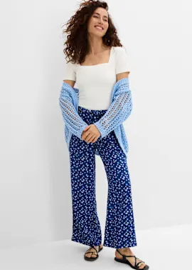 Weißes Oberteil, blaue Musterhose, hellblaue Strickjacke und schwarze Sandalen.