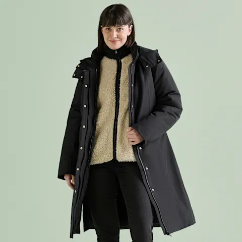Warmer schwarzer Mantel über beiger Fleecejacke und dunkler Hose.