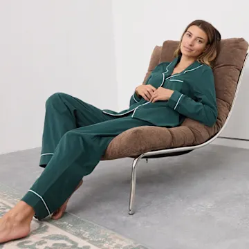 Sie trägt einen bequemen, grünen Pyjama mit weißen Details, entspannt auf dem Sessel.