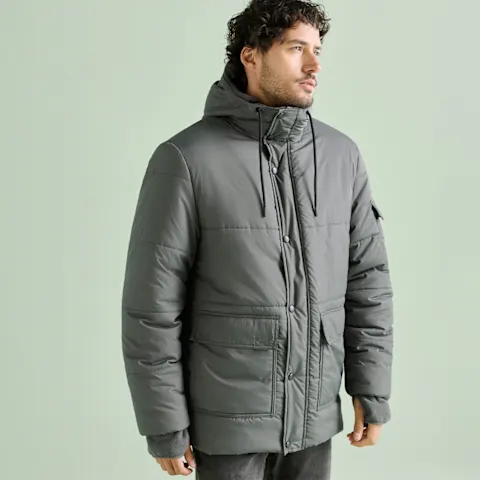 Graue wattierte Jacke mit Kapuze über dunkler Jeans.