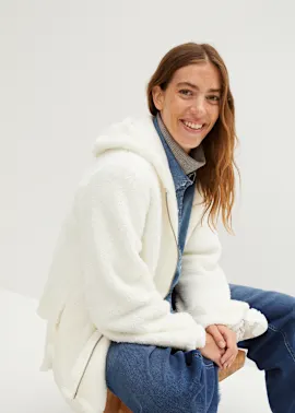 Weiße Teddyjacke über Denimhemd und Rollkragenpullover, dazu blaue Jeans.