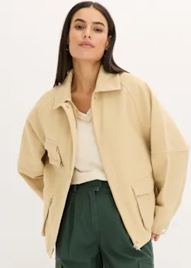 Lässige beige Jacke über hellem Top, kombiniert mit dunkelgrüner Hose.