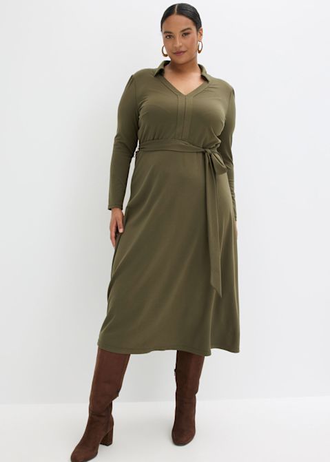 Olivgrünes Kleid mit V-Ausschnitt und Gürtel, kombiniert mit braunen Stiefeln.