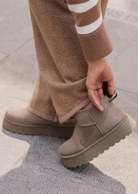 Brauner Pullover, weite Hose und graue Plateaustiefel prägen den komfortablen Look.