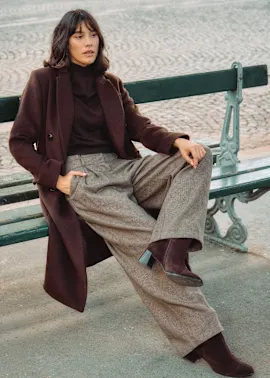 Langer brauner Mantel, Rollkragenpullover und weite Tweedhose.