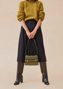 Senfgelber Pullover, schwarzer Midirock, braune Stiefel und elegante Handtasche.