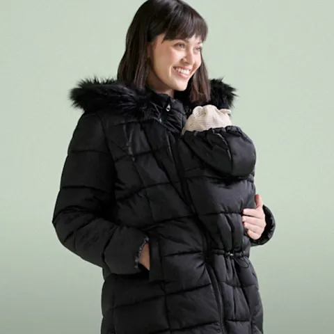Frau trägt eine warme schwarze Winterjacke mit Babytrageeinsatz und Pelzbesatz.