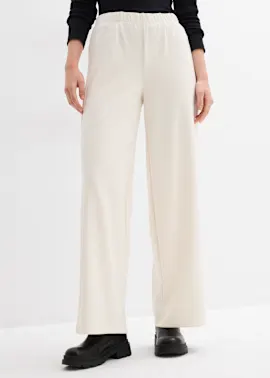 Cremefarbene weite Hose mit schwarzem Oberteil und klobigen schwarzen Schuhen.