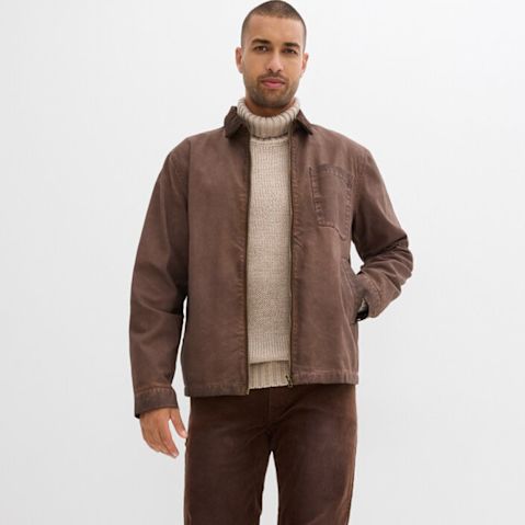 Braune Lederjacke, beiger Rollkragenpullover und passende Hose.