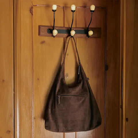 Eine stilvolle braune Tasche hängt an der hölzernen Wandgarderobe mit Messinghaken.