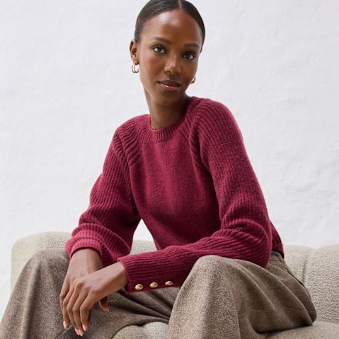 Roter Pullover mit beiger Hose auf hellem Sofa.