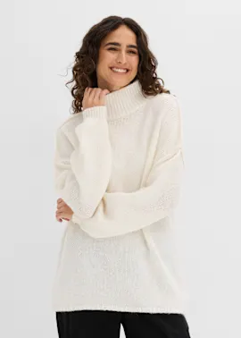 Sie trägt einen bequemen, cremefarbenen Rollkragenpullover mit lockerem Strickmuster.