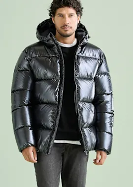 Moderne schwarze Glanz-Steppjacke mit Kapuze, schwarzer Pulli, dazu graue Jeans.