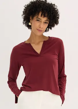 Bordeauxrotes Langarmshirt mit V-Ausschnitt und weiße Hose ergeben ein stilvolles Outfit.