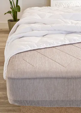 Gesteppte Decke und das gemusterte Laken auf dem Bett.