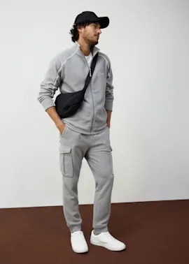 Lässiger grauer Trainingsanzug mit Reißverschlussjacke und weißen Sneakern.